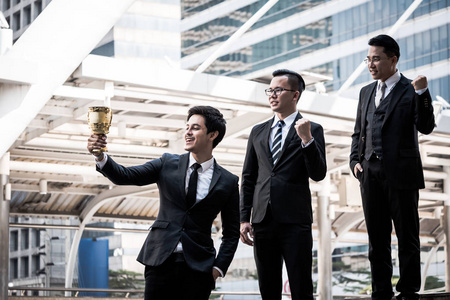 快乐的亚洲商界人士与金奖杯杯为他们的赢家在商业项目。团队合作和成功理念