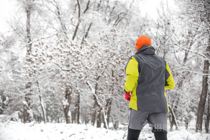 冬天的时候在森林里奔跑的人。男子身穿运动衫在公园冬季慢跑
