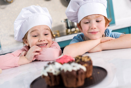 快乐的孩子在厨师帽子看着美味的蛋糕前景