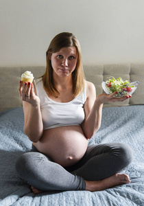 孕妇拿着西红柿和美味的甜蛋糕在她的手绿色沙拉
