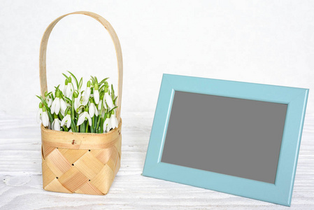 空白相片框架与春天雪花莲花在一个柳条篮子在白色木桌上