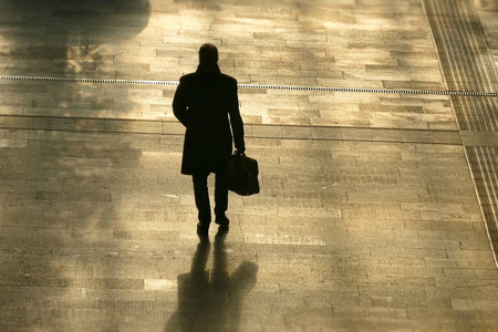 孤独的男人的剪影拿着一个袋子往前走向后看照片