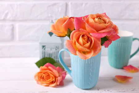 花静物。蓝色杯上的鲜橙玫瑰, 白色的木质背景, 白色的砖墙。文本位置