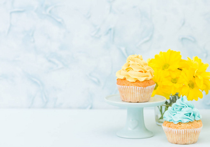 甜黄色奶油装饰的蛋糕和黄色菊花花束在复古破旧别致的花瓶在蓝色粉彩背景