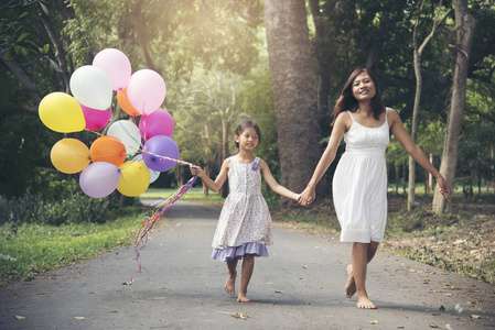 我喜欢妈妈在母亲节的时候一起呆在一起。可爱可爱的女孩拿着气球, 母亲走在公园的路上。家庭理念