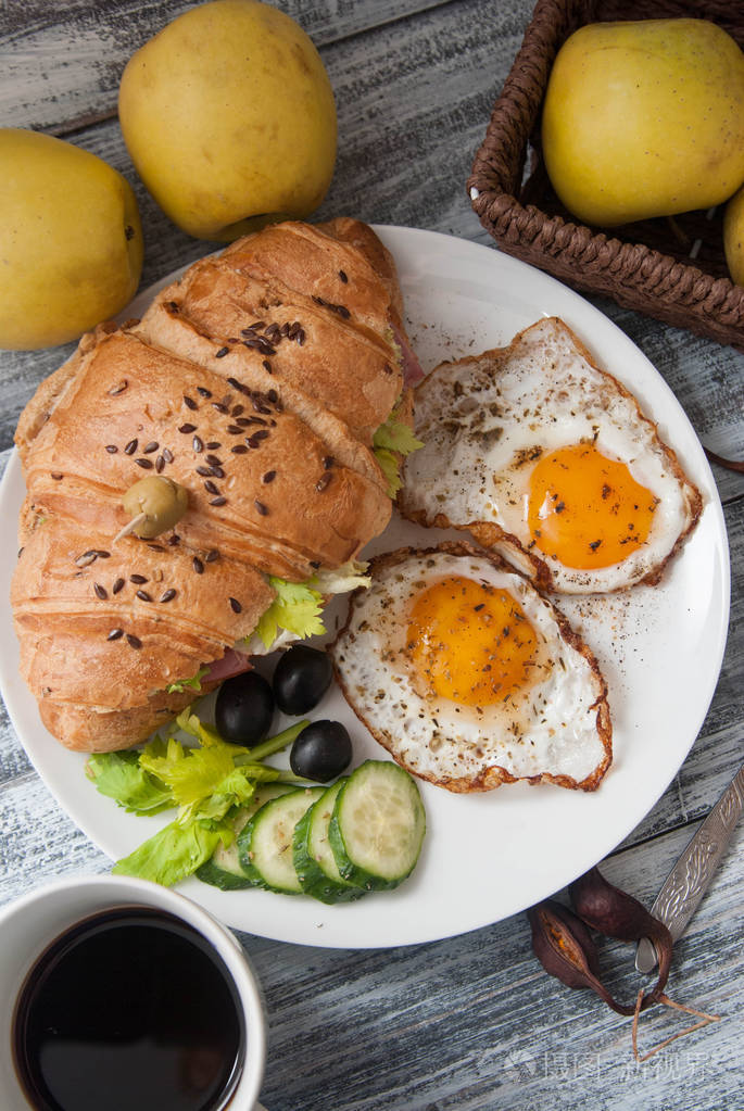 早餐食品煎蛋和羊角面包三明治配黄瓜橄榄和杯咖啡篮子里有苹果垂直