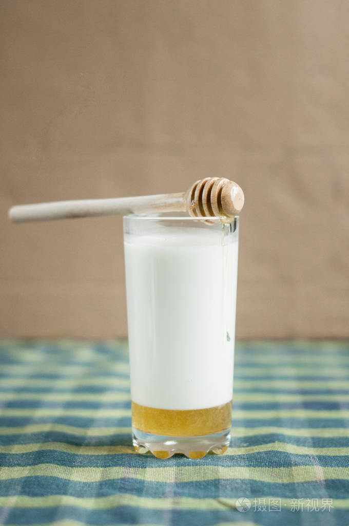 一杯带蜂蜜的牛奶和桌布上的木勺