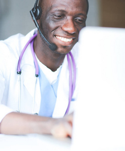 年轻的男医生在诊所桌上使用计算机时戴耳机的画像。医生