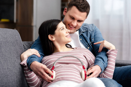 快乐的年轻夫妇戴着耳机在家里的腹部