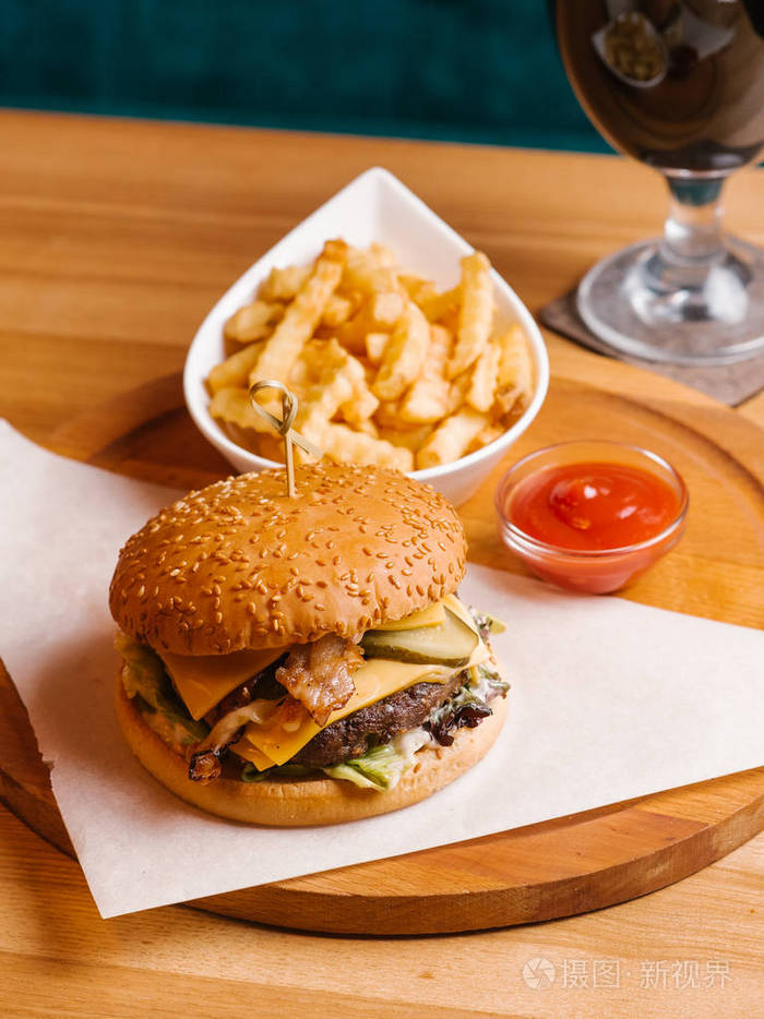 特写芝士汉堡与串法式薯条在白色碗与蕃茄酱在木盘子上服务与黑啤酒