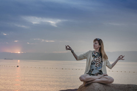 女孩在海的岩石之上和傍晚天空与日落和蓝色云彩