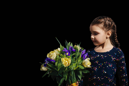 她手里捧着鲜花的小女孩。幸福的概念, 人, 孩子, 童年。工作室照片在黑色背景。文本空间