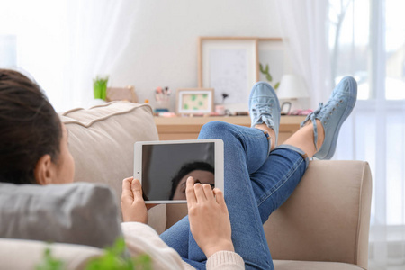 年轻妇女使用平板电脑, 而在沙发上休息在家
