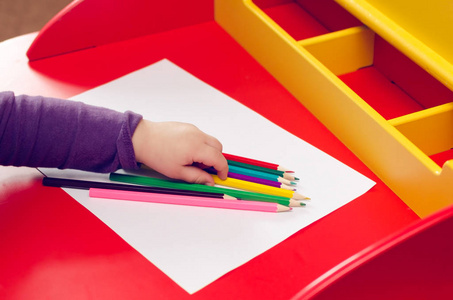 孩子们的手用彩色铅笔涂在一张红色桌子上的白纸上。