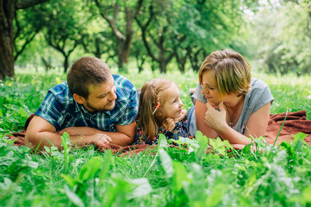 年轻快乐家庭三躺在毯子上的公园里玩得开心。快乐的育儿理念。小女孩与父母在户外