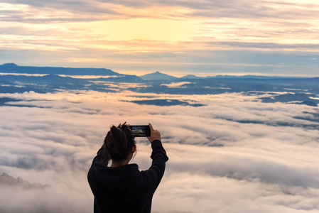旅行者的女人戴着帽子使用智能手机拍摄美丽的山景观与雾海