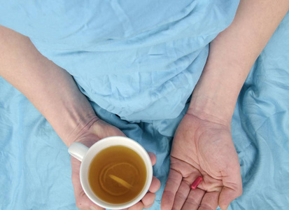 流感季节。病人手中拿着药丸和杯子的热茶在床上。在家中虐待白种人的特写