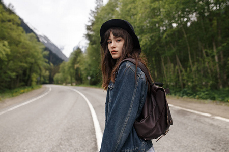 妇女旅行者与背包拿着帽子和看在惊人的山和森林, 流浪旅行概念, 空间为文本, 大气史诗时刻