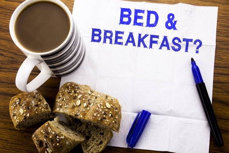 手写的文本显示早餐。假日旅行的商业概念在木质背景的纸巾上写上与笔面包健康咖啡在餐厅