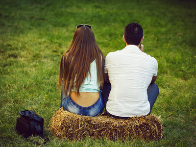 女孩和男人坐在干草捆在绿色草地上