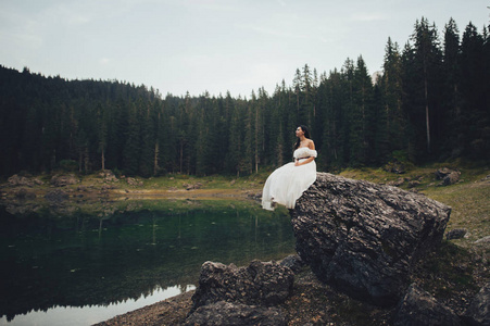 穿着婚纱的年轻女子坐在岩石与山森林在背景上
