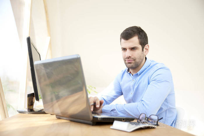 年轻销售人员的肖像坐在笔记本电脑和电脑前, 并在线工作