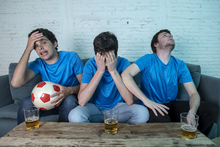 一群年轻的足球球迷在蓝色 t恤衫失望, 而看足球比赛在沙发上在家