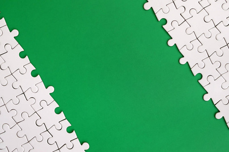 在绿色塑料表面的背景下折叠的白色拼图拼图碎片。用于文本的复制空间的纹理照片