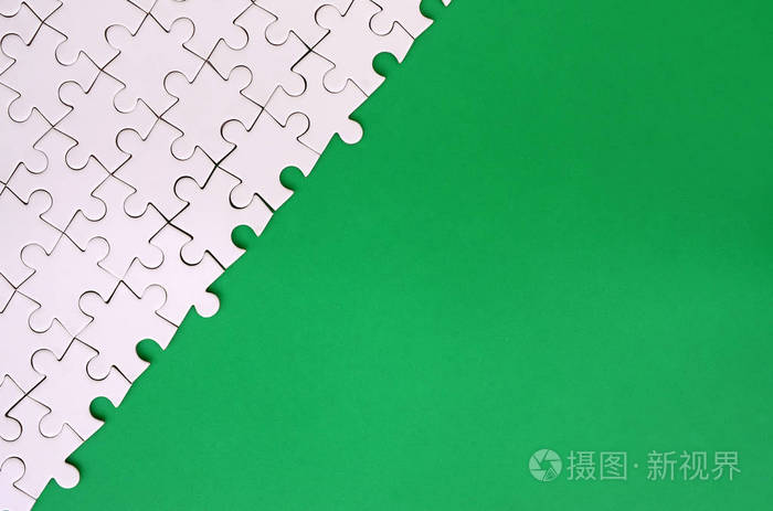 在绿色塑料表面的背景下折叠的白色拼图拼图碎片。用于文本的复制空间的纹理照片
