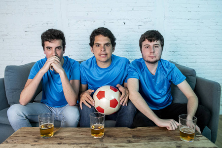 一群年轻的足球球迷在蓝色 t恤衫失望, 而看足球比赛在沙发上在家