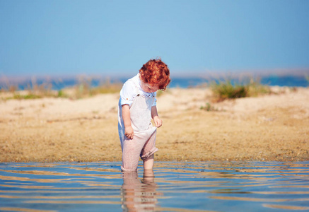 可爱的红发学步婴儿男孩在清晨的湖水中浸泡衣物