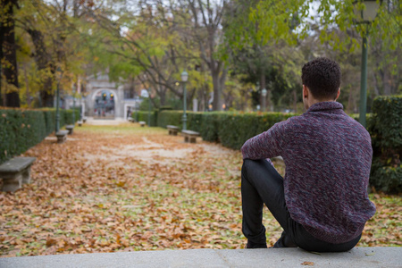 一个体贴的年轻人坐在楼梯上的秋天公园, 看着远离