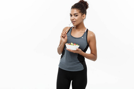 健康和健康的概念美丽的美国非洲女士在健身衣上节食吃新鲜的沙拉。在白色背景上被隔离