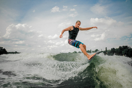 英俊的运动的家伙 wakesurfing 在棋盘上对天空