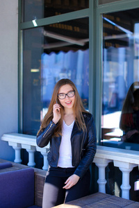漂亮的女孩在眼镜 talkingking 的智能手机在街头咖啡馆