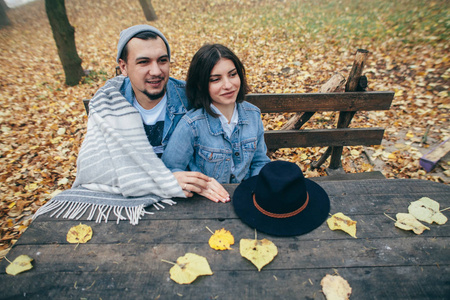 愉快的夫妇涂层与毯子和坐在长凳在公园