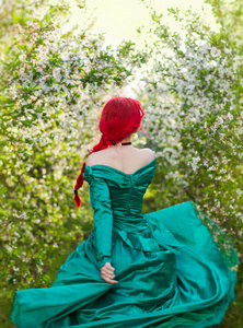女孩在一个长绿色礼服在一个盛开的杏花园的帽子
