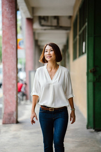 中国年轻的亚洲妇女沿着新加坡亚洲的走廊散步。她穿着巧妙的商业休闲, 短发和微笑, 她漫步在走廊上