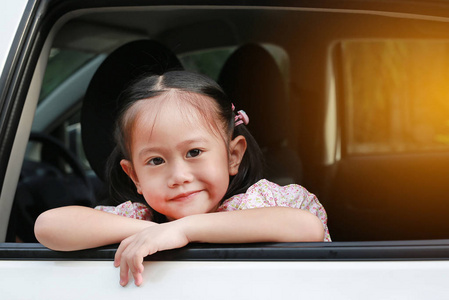 可爱的小亚洲女孩看着相机从窗口的汽车与阳光光线