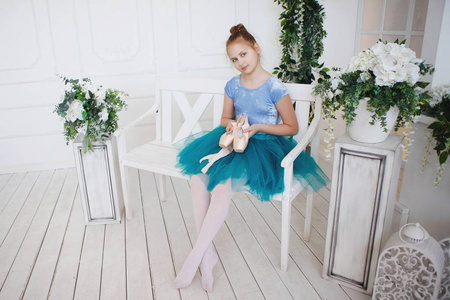 一个年轻的芭蕾舞演员在蓝色的裙子与粉红色的指出坐在一个白色的木凳上