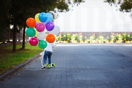 快乐的男孩与一束彩色 balloonsriding 一辆滑板车。后退视图