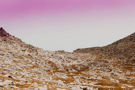 柔和地倾斜的丘陵和柔和的颜色。粉红色的天空下的岩石。旅途入山国家