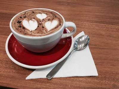 白色陶瓷杯, 热咖啡饮料在一张木桌上的红盘子里, 用一把金属勺子放在白色餐巾上。