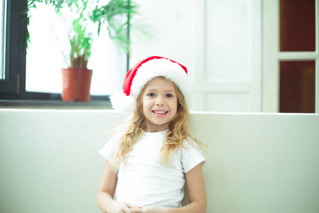 微笑着美丽的金发碧眼的小女孩坐在家里的沙发上, 看着相机。新年和圣诞节