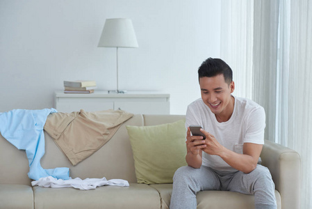 英俊的亚洲年轻人在家休息时给朋友发短信
