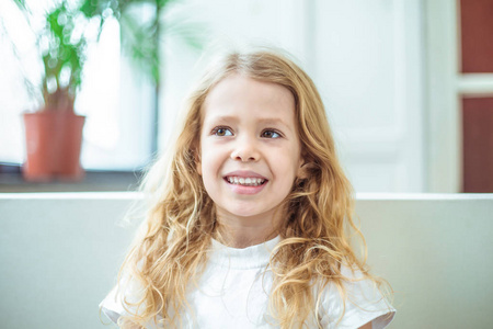 一个美丽的微笑的金发小女孩的肖像。坐在家里沙发上的孩子