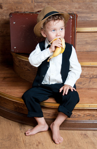 可爱的小男孩坐在台阶上，他手里的香蕉