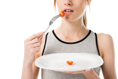 苗条的女人吃小樱桃西红柿在白色的分离拍摄
