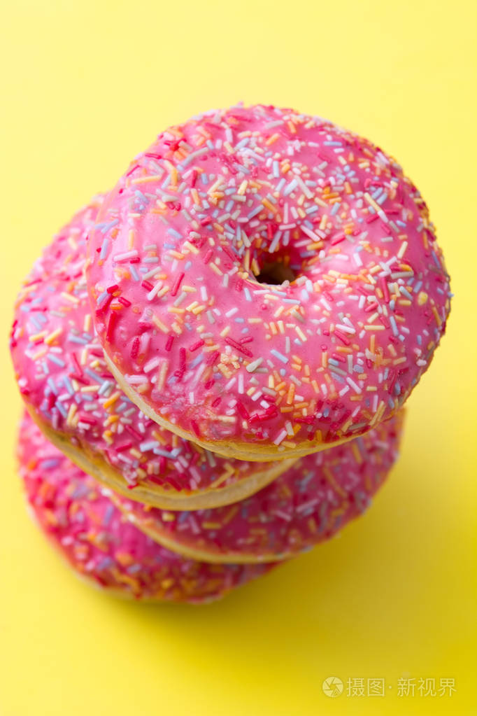 粉红色的磨砂甜甜圈与彩色洒在黄色背景