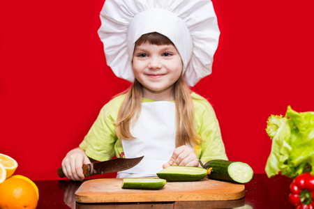 快乐的小女孩在厨师制服在厨房切开菜。小厨师素食.烹调过程概念